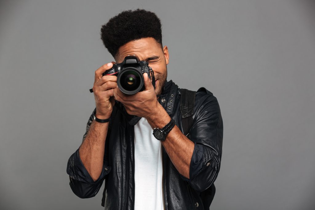 Passion et Précision Photographe africain élégant en veste de cuir prenant une photo avec un appareil photo professionnel.