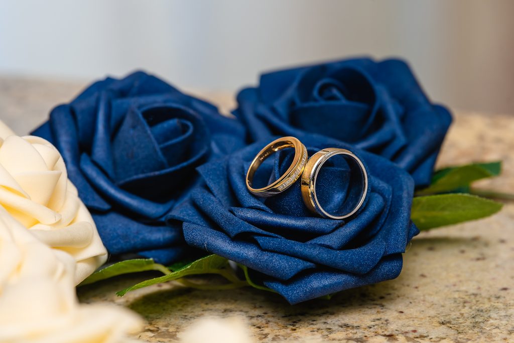 Contraste de Couleurs et d'Engagement Deux alliances en or posées sur des roses artificielles bleues et crème, symbolisant l'union et l'engagement.
